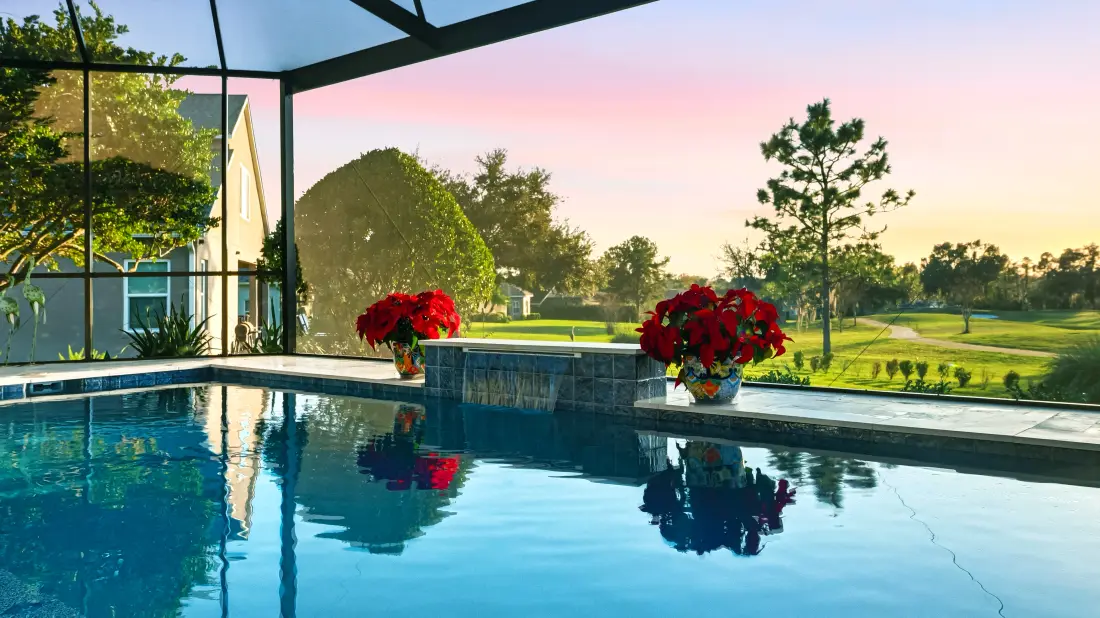 Screened lanai pool and spa overlooking a golf course at dusk.