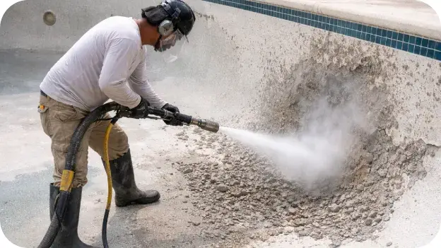 Worker hydro-blasting the interior surface of an empty pool.