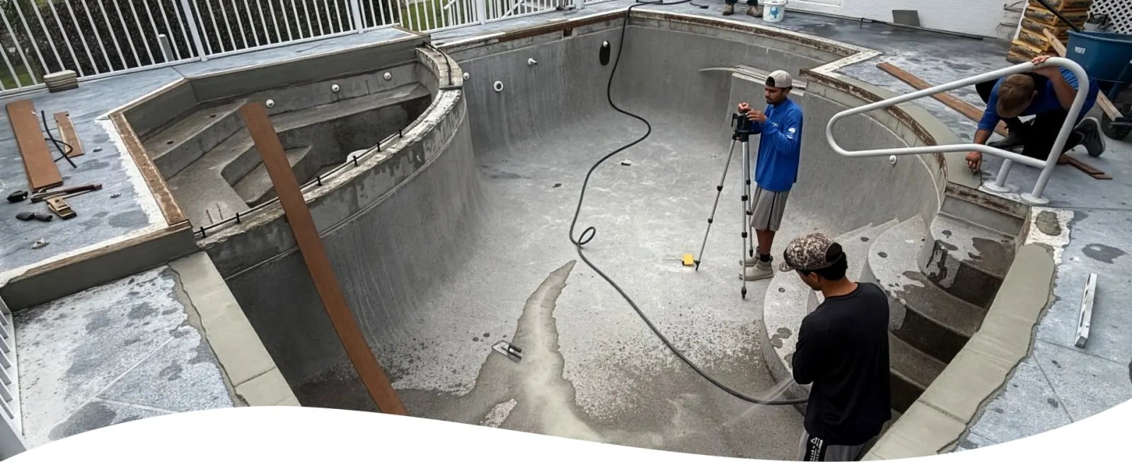 Workers performing structural rebar work in an empty pool beneath a screen enclosure.