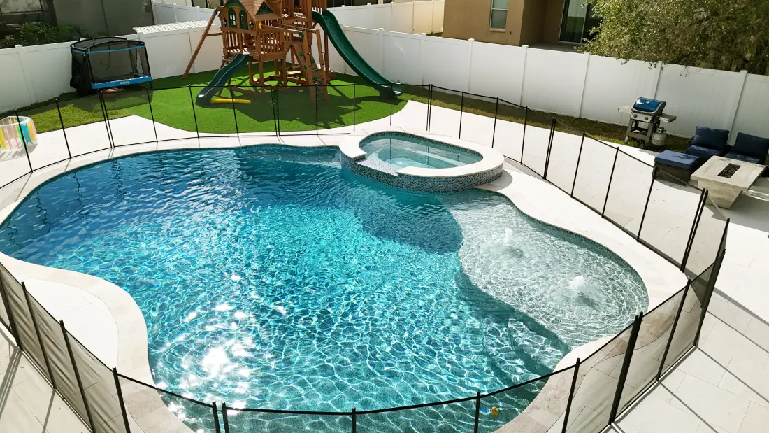 Freeform pool with an attached spa and a child's playset in the backyard.