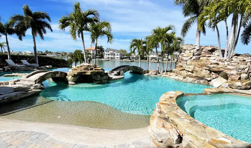 Freeform pool with a rock waterfall feature and tropical landscaping.