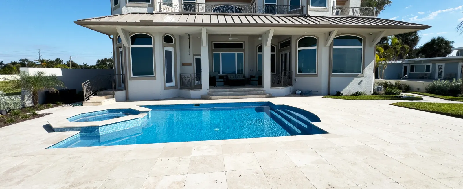 Rectangular pool with a square raised spa and paver decking, ocean view in the background.