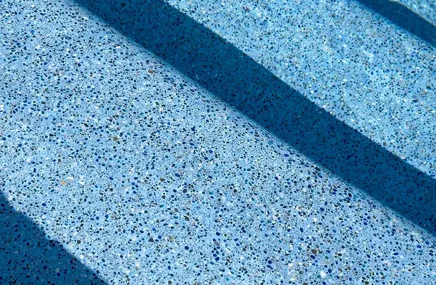 Close-up of the pool's pebble-finish wall with a glass tile accent band.