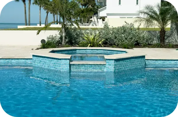 Close view where the blue-tiled raised spa meets the pool, palm trees behind.