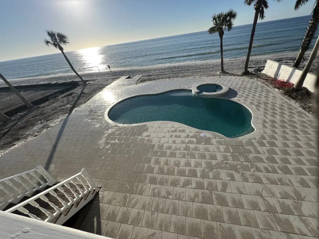Elevated view of a freeform plunge pool set into paver decking beside a beach access stairway, ocean in the distance.