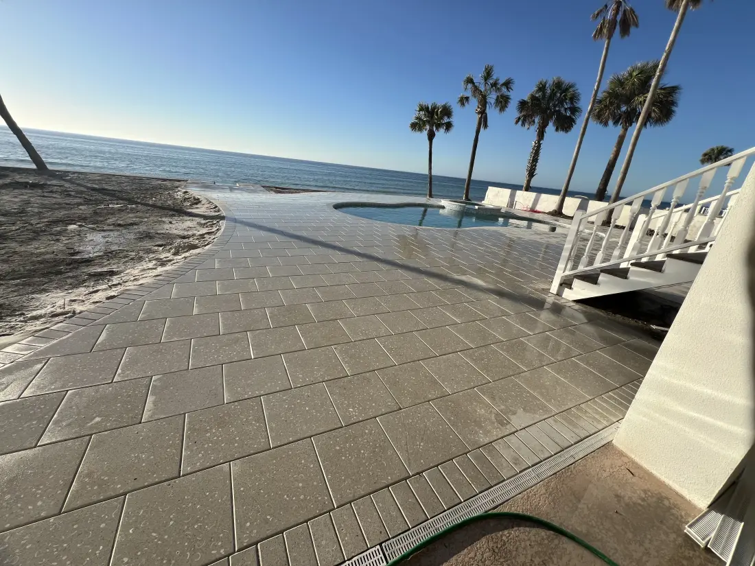 Paver walkway leading to a beach stairway, ocean and palm trees in view.