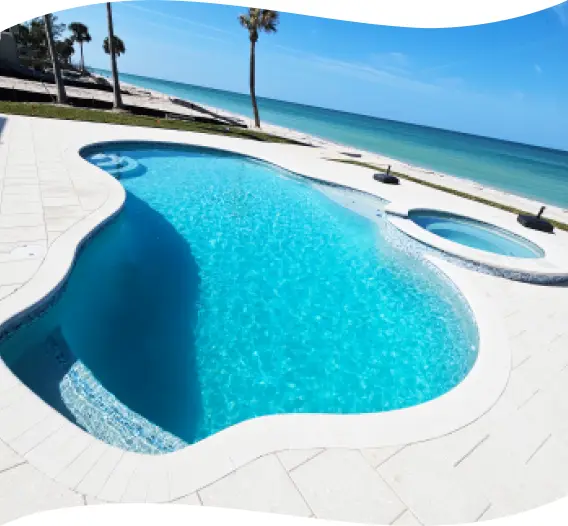 Finished kidney-shaped pool with a round raised spa and paver decking on a beachfront lot.