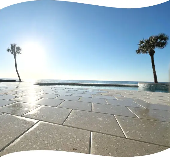 Beachfront pool deck at sunset, wet pavers reflecting the sky, palm trees silhouetted.