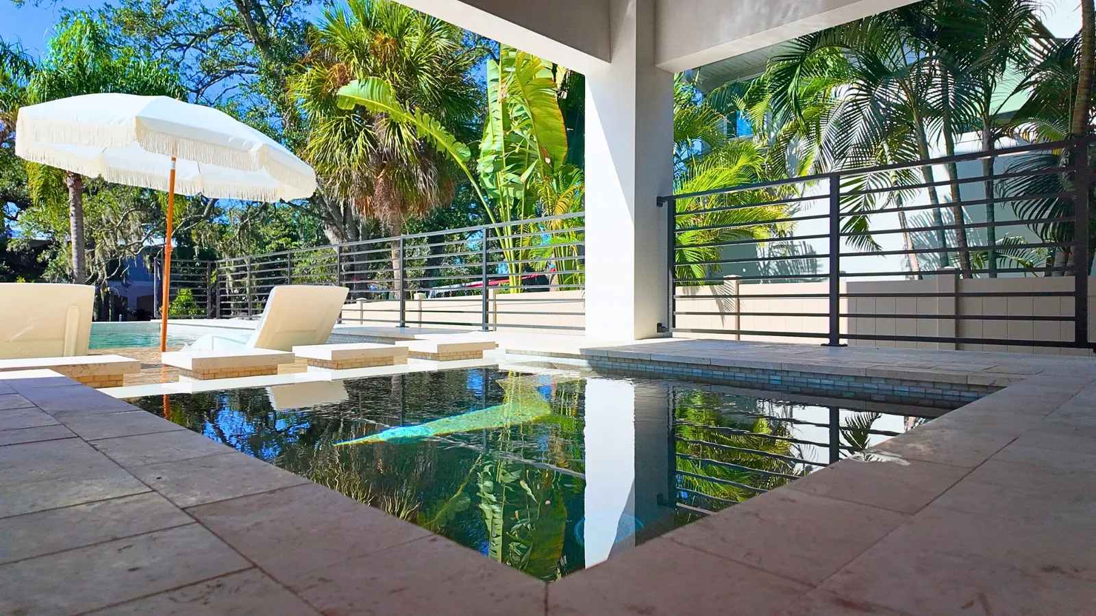 The stepping stones and sunshelf across still water, the green glass waterline tile banding the pool edge at the right.