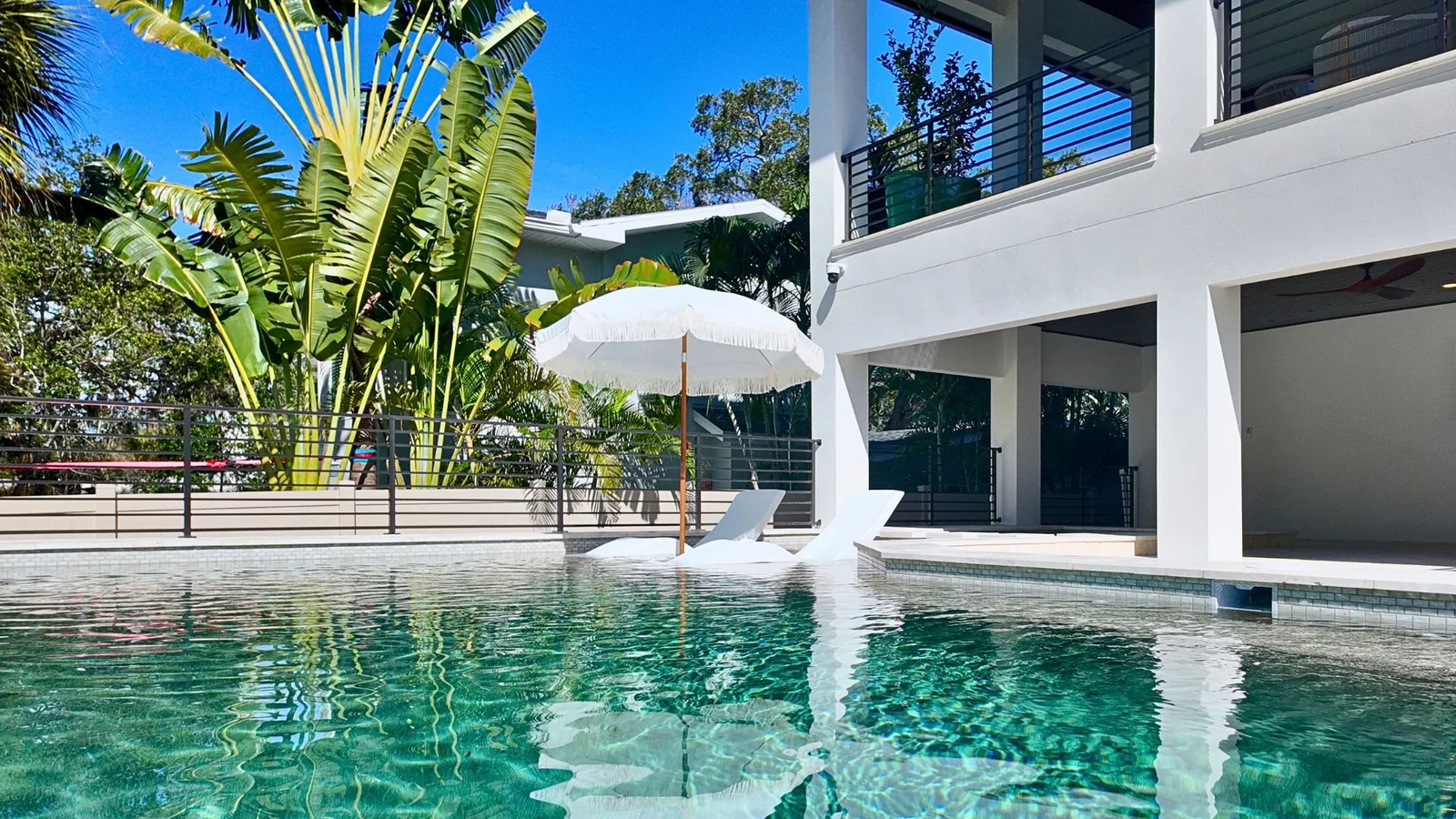 Water-level view across the pool toward the house, the bench seating and its glass tile band running along the far edge.