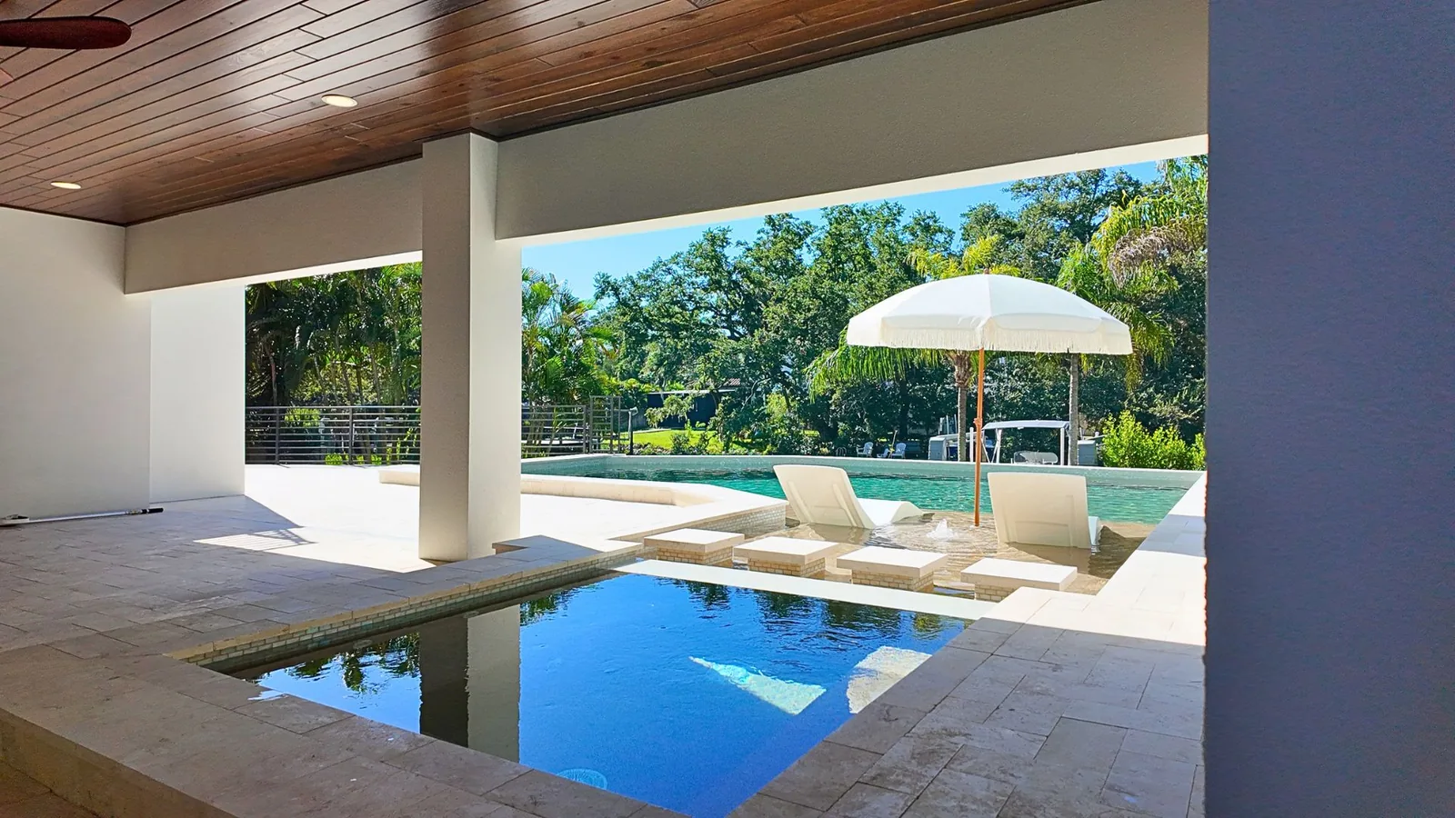 The view out from under the wood-clad lanai: the glass-tiled spa in the foreground, the sunshelf and the rest of the pool beyond it.
