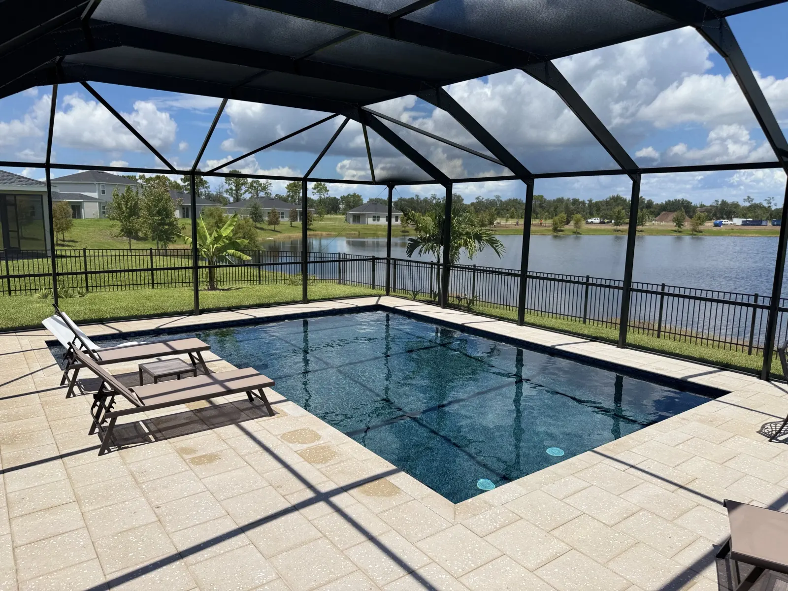 Screened lanai pool with loungers and a pond view beyond the pool cage.