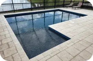 Rectangular pool with a notched bench seat and paver decking inside a screened enclosure.