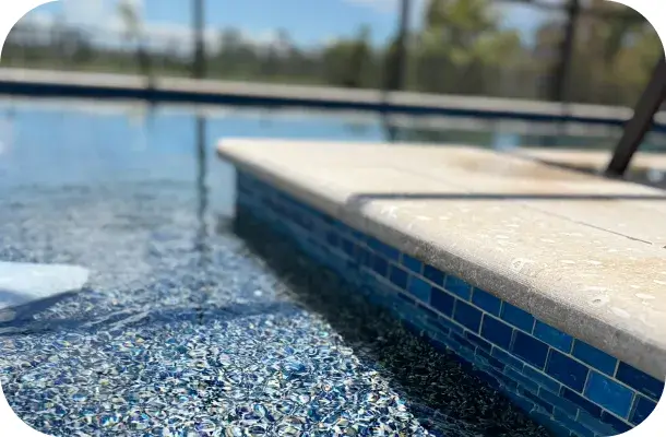 Close-up of the pool's paver coping and blue glass tile waterline band.