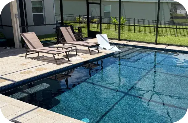 Rectangular pool with notched bench seating, loungers, and screen enclosure, pond in the background.