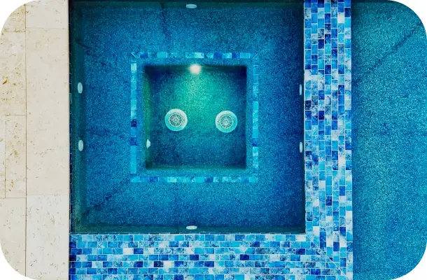 Top-down view into a square raised spa with blue tile and two water jets.