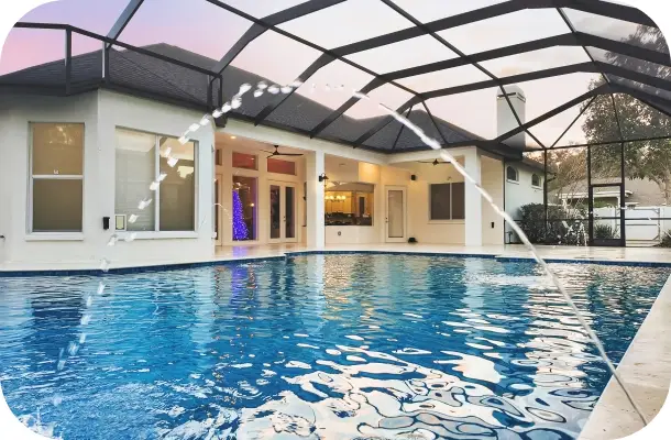Pool and screened enclosure at dusk with the home lit up behind, colorful evening sky.