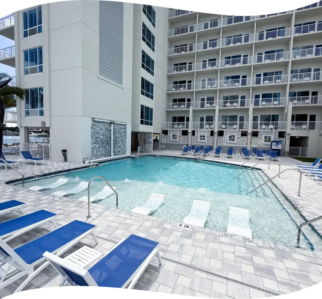 Pool deck with rows of lounge chairs and a marina view under a clear sky.