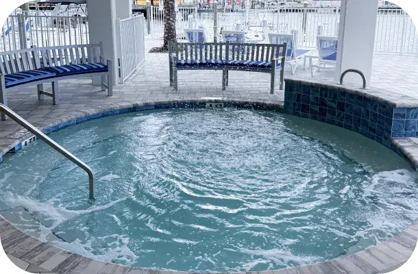 Close view of a circular spa built into the deck, water bubbling, cabana structure behind.