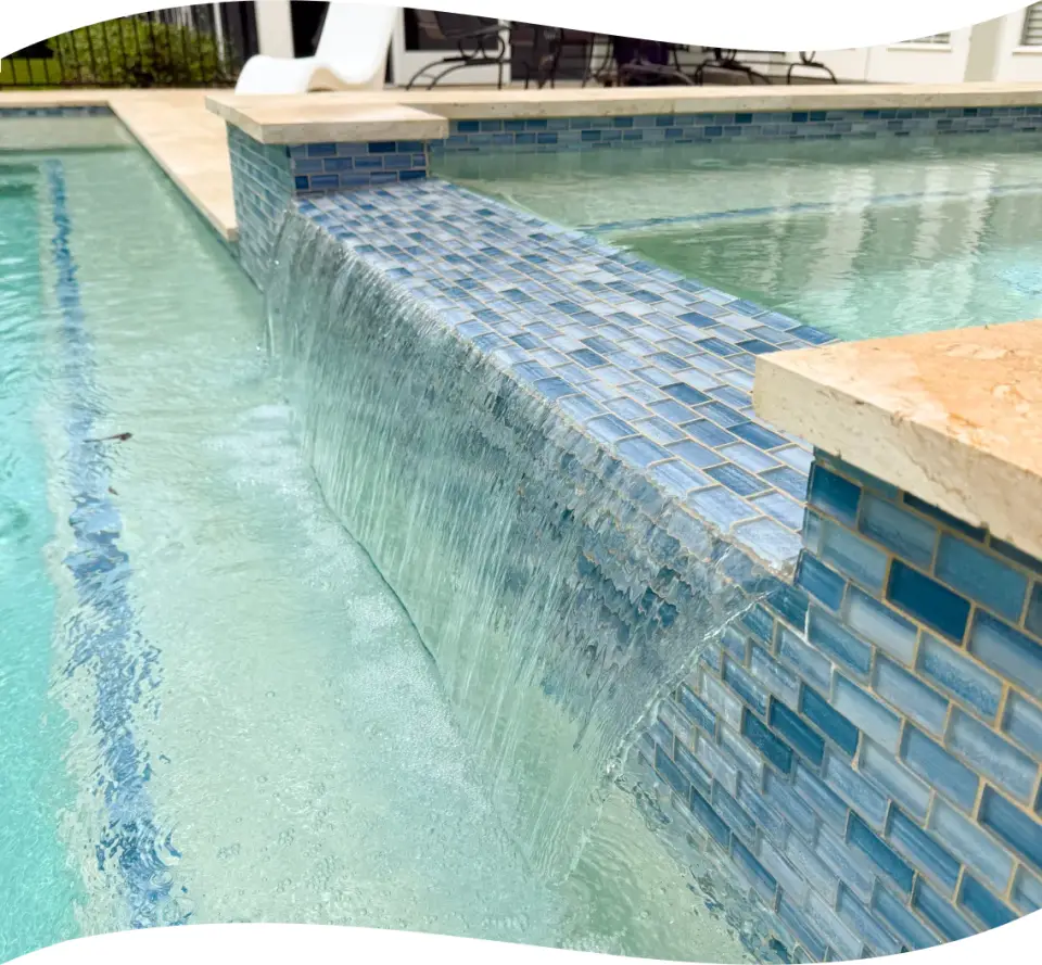 Close-up of the raised spa's glass-tile wall with water spilling into the pool below.
