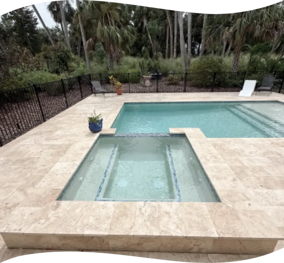 Elevated view of a rectangular pool and raised spa behind a black safety fence, wooded lot.