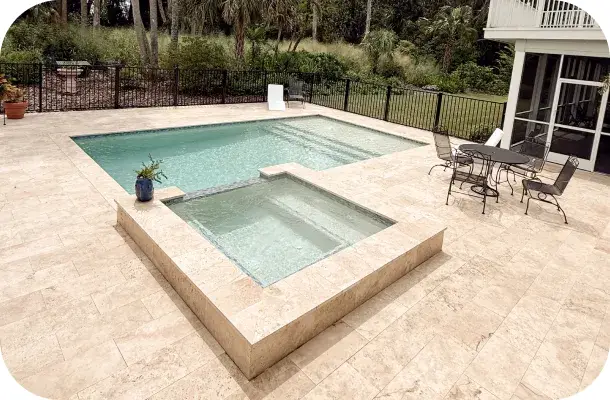 Wide view of the pool, spa, and patio furniture with the house and wooded backyard behind.