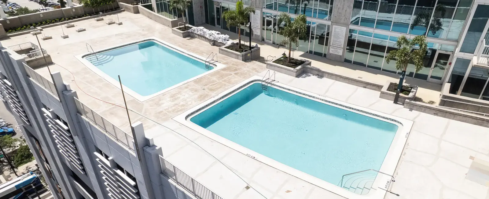 Aerial view of two rectangular pools on a high-rise rooftop with the city skyline behind.