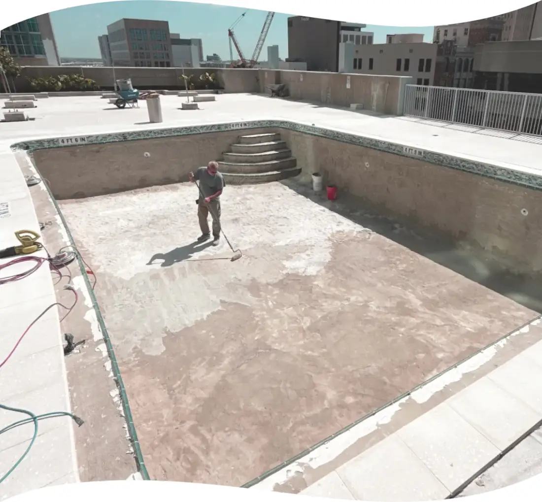 Worker finishing the concrete shell of an empty rooftop pool during construction.