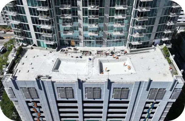 Aerial view of a high-rise rooftop under construction with two pool cutouts and cranes visible.