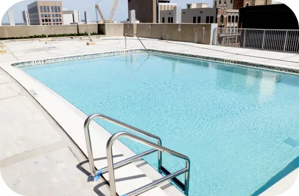 Finished rectangular rooftop pool with a ladder rail and city building in view.