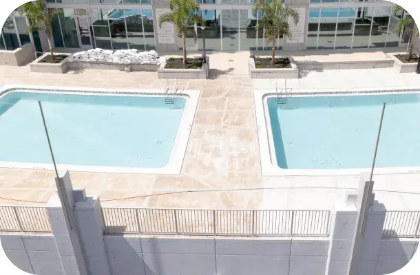 Aerial view of two finished rectangular rooftop pools separated by planters, city skyline behind.