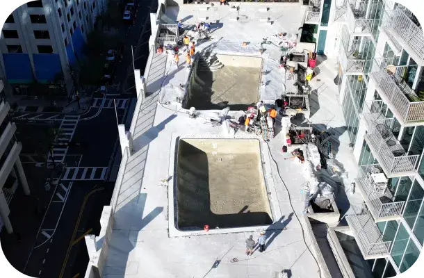 Aerial construction-phase view of two rooftop pool shells being formed, workers on site.