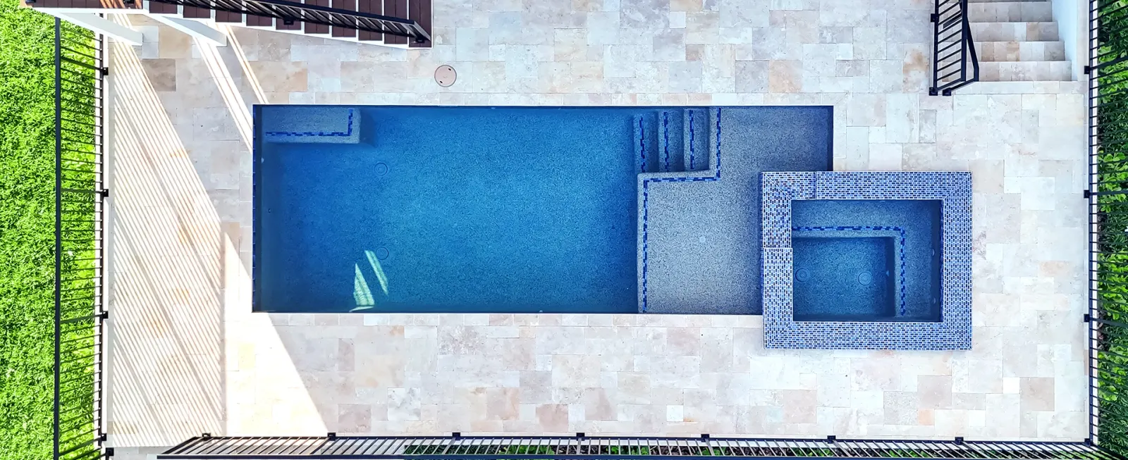 Top-down view of a rectangular pool and raised spa built on an elevated paver deck.