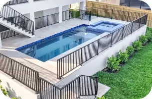 Ground-level view of the raised pool deck and spa alongside the home's black-railed balcony.