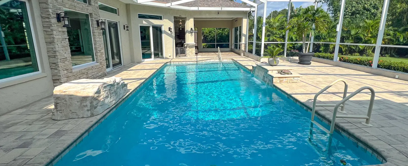Long lap-style pool inside a screened lanai with travertine decking along the home.