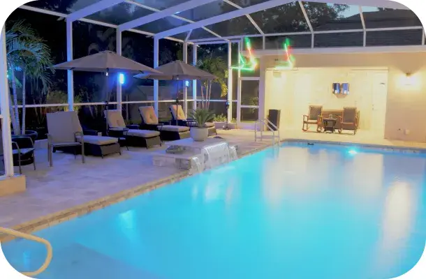 Pool and spa lit at dusk inside a screened lanai with an outdoor lounge and string lights.