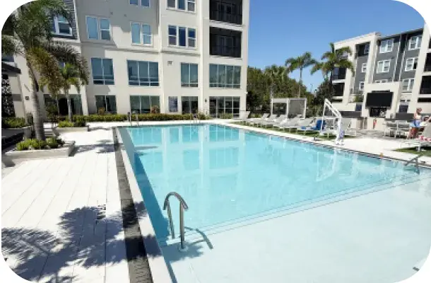 Community pool deck with lounge chairs facing the multi-story building.
