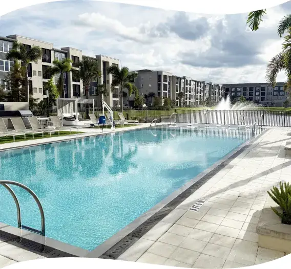 Community pool with a fountain feature at the far end, building and palms behind.