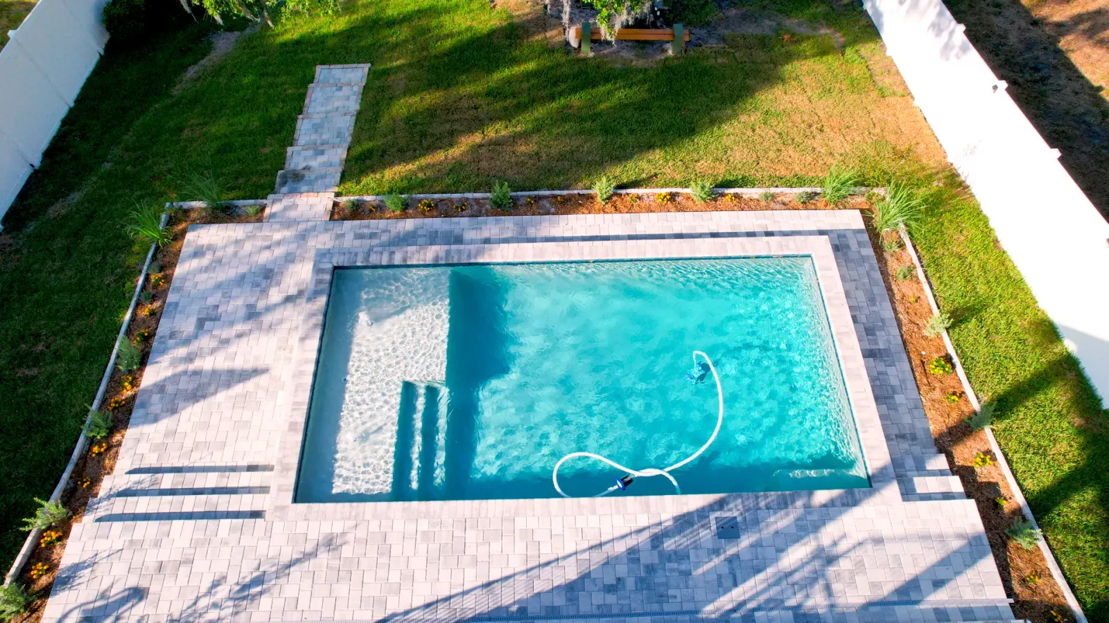Finished rectangular pool with paver decking and a garden hose on the deck.