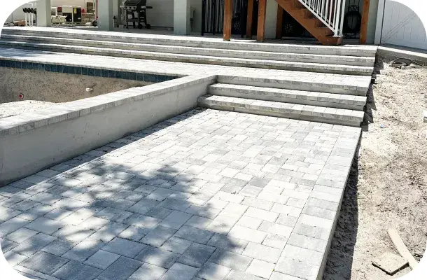 Paver decking being installed around the pool during construction.