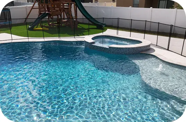 Close view of the freeform pool's water feature with the playset visible behind the fence.