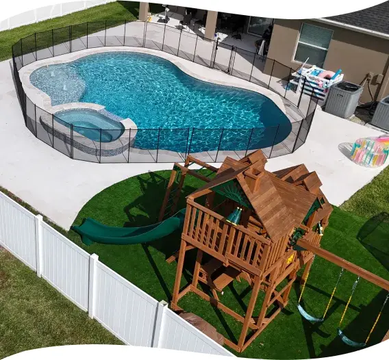 Wide view of the backyard with the freeform pool, spa, playset, and privacy fence.