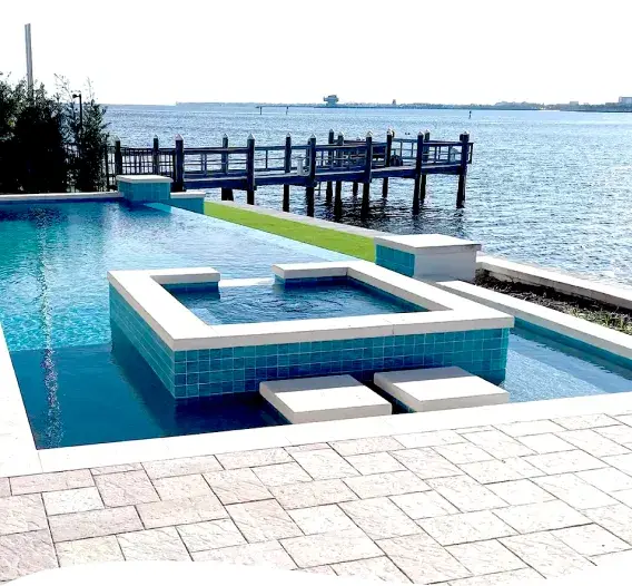 Pool and raised spa on a waterfront lot with a canal and dock visible behind.