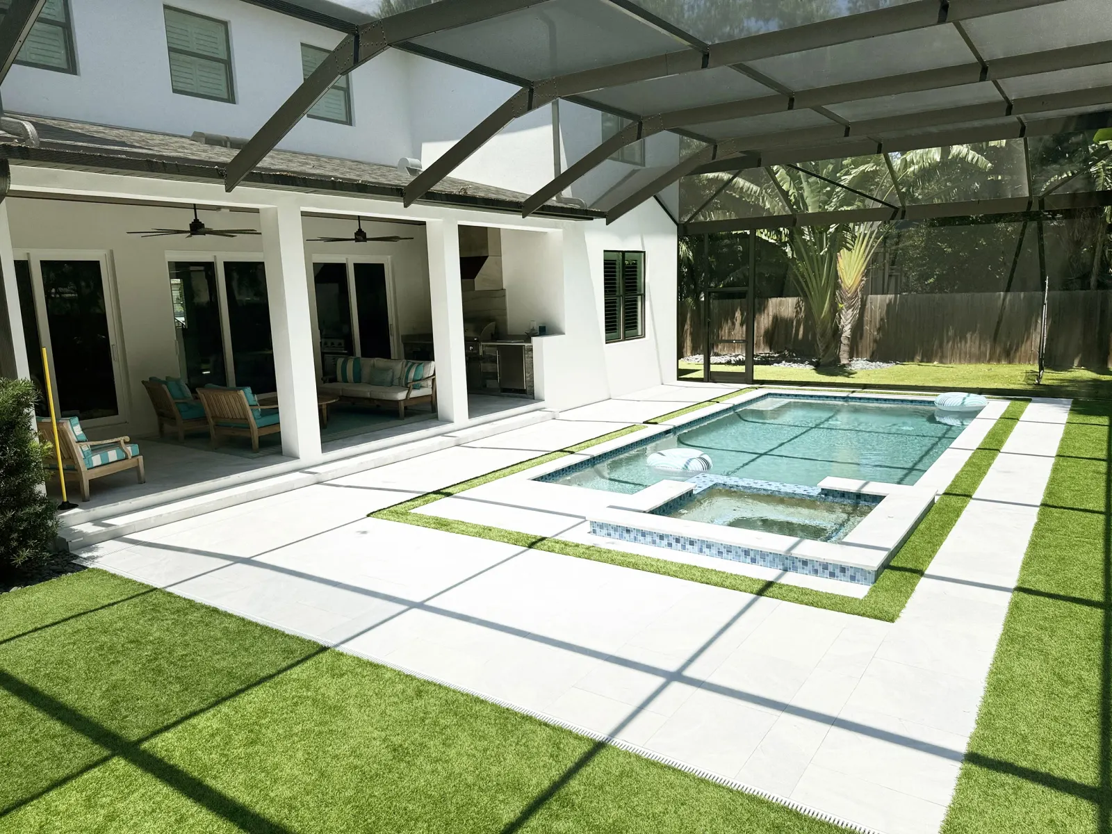 Aerial view of a modern home with a rectangular pool, raised spa, and artificial-turf accents under a covered lanai.