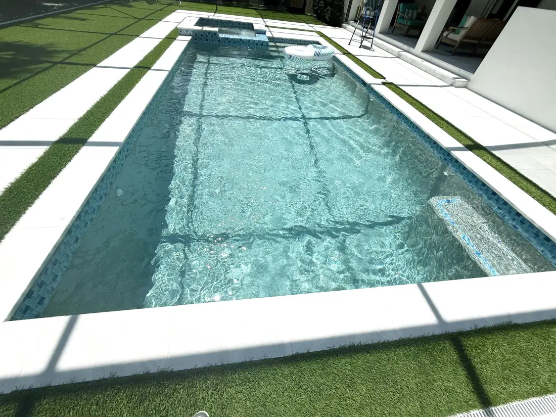 Long rectangular lap pool with a raised spa at one end, bordered by artificial turf.