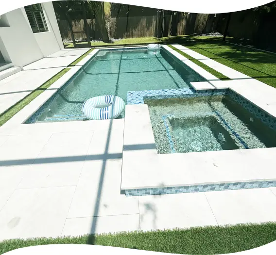 Rectangular pool with a raised spa and a pool float, artificial-turf border.