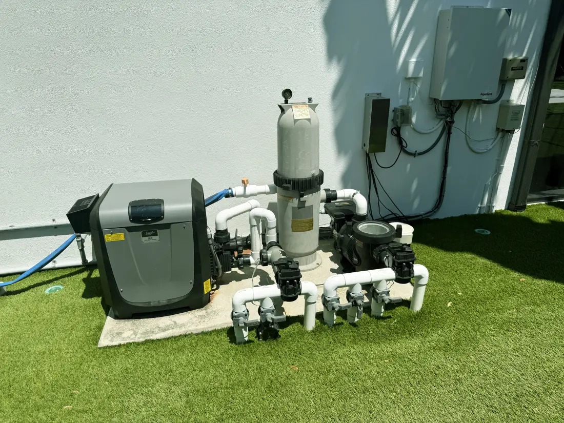 Pool equipment pad with pump and filter installed on artificial turf beside the home.
