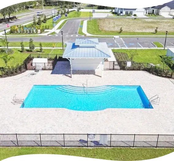 Aerial view of a curved-edge community pool beside a small clubhouse building and parking lot.