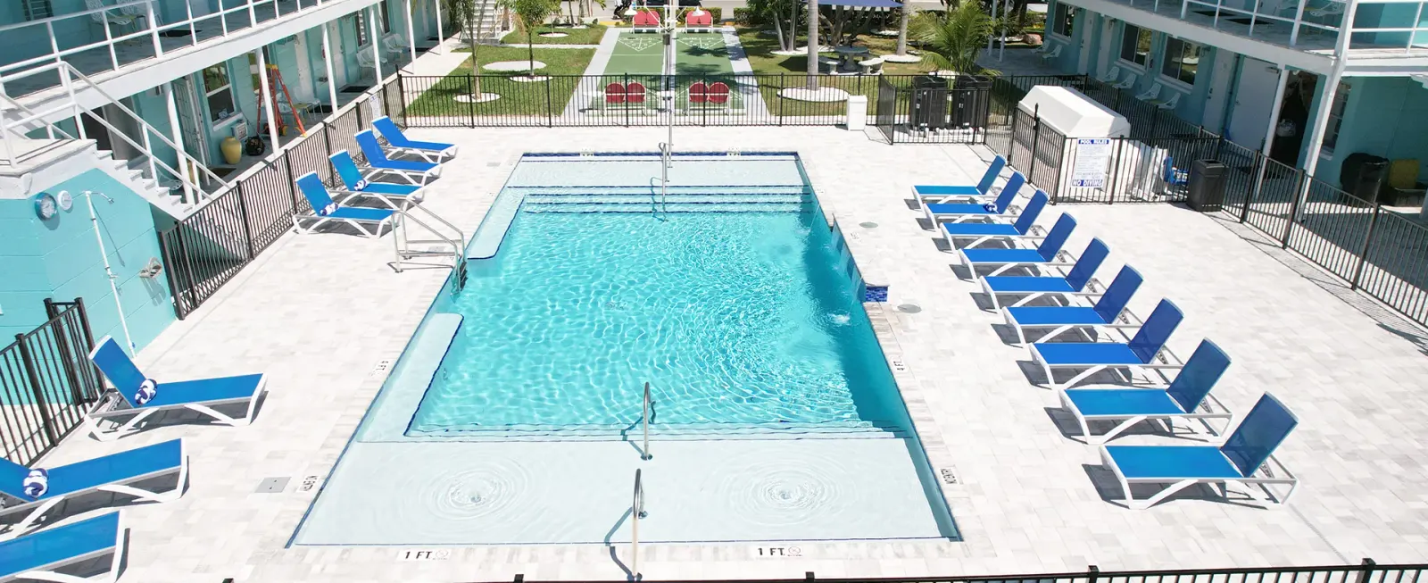 Aerial view of a rectangular pool with lounge chairs beside a canal, low-rise building nearby.
