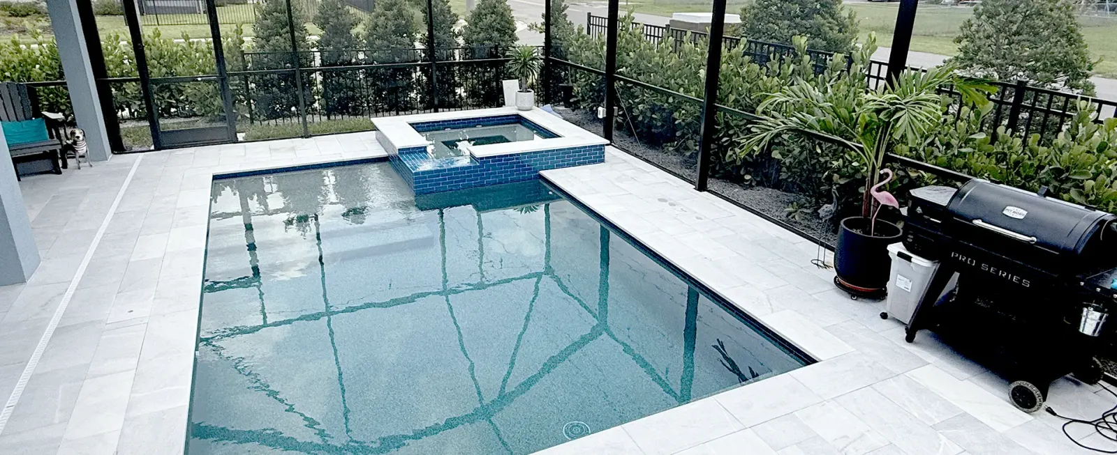 Screened lanai pool with a blue-tiled raised spa and paver decking.